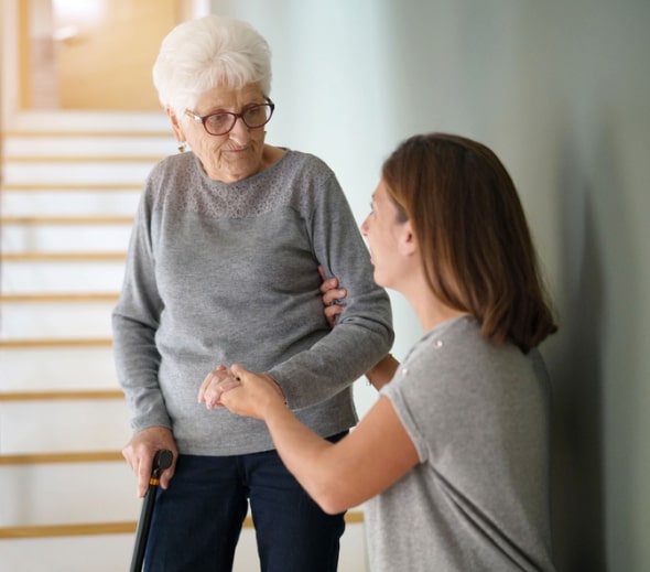 A caregiver helping an elderly lady down the stairs