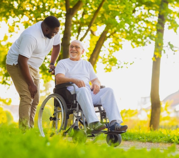 Caretaker taking an elderly man in a wheelchair on a stroll through the park