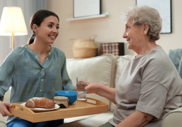 Caregiver bringing food to elderly woman
